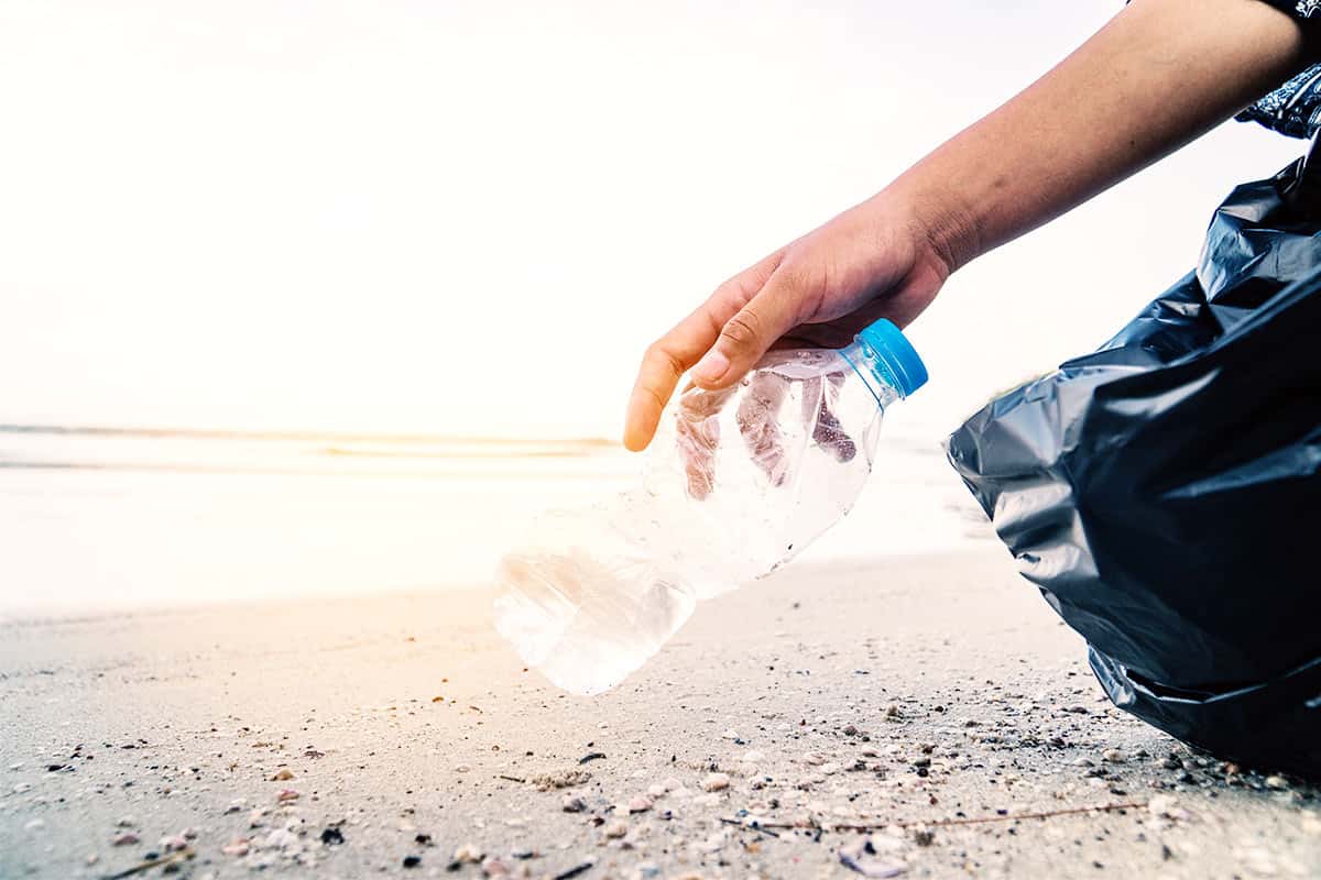 Plastikflasche am Strand © AdobeStock Mensch hebt Plastikflasche am Strand auf